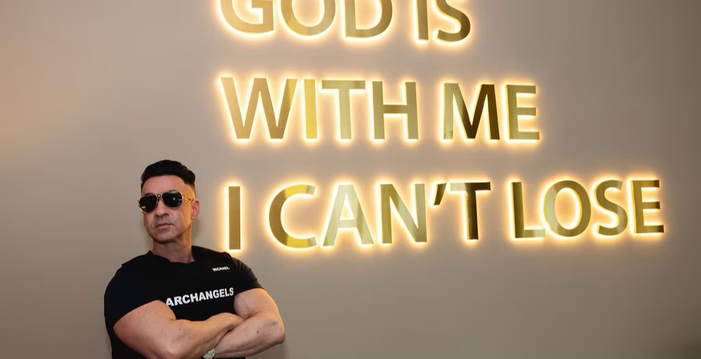 Mike Sorrentino, Founder, beneath the 'God is with me, I can't lose' wall